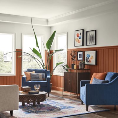 Bright Living Room Space with two blue chairs, round coffee table, decor on the walls, plant, and windows.